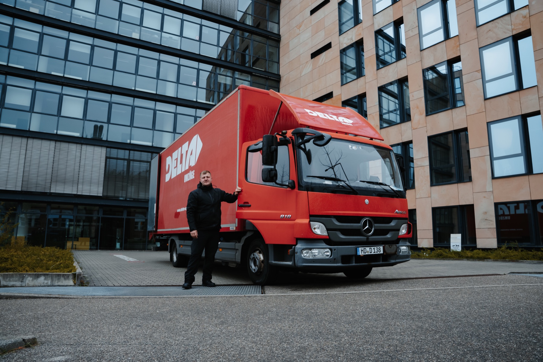 Eine Person neben einem roten Umzugswagen von DELTA Umzüge vor einem Gebäude.